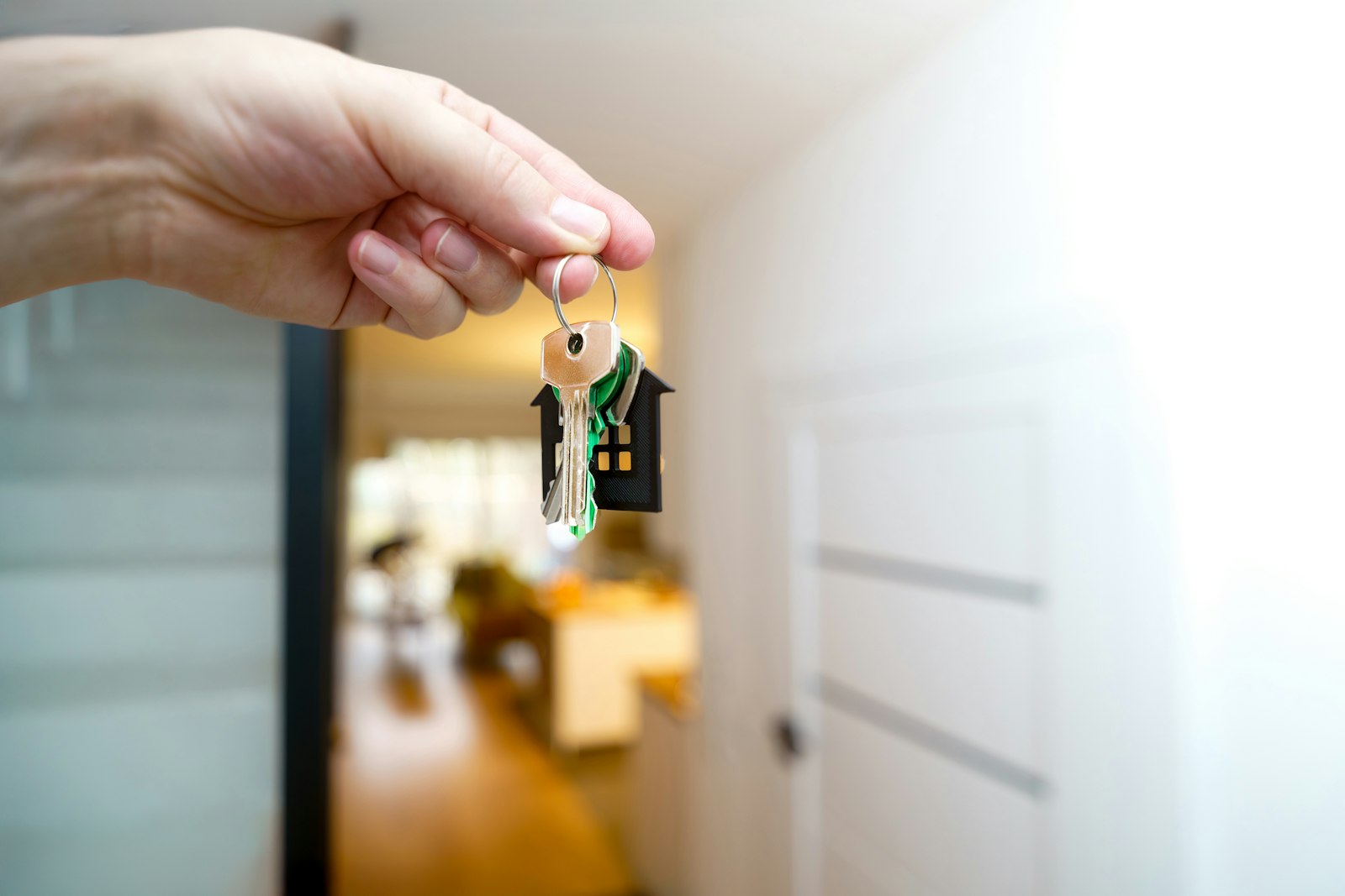 Hand hält einen Schlüsselbund mit Haus-Anhänger vor einer geöffneten Wohnungstür